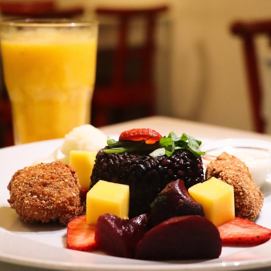 Prato de arroz negro com beterraba, morango e rúcula, com um copo de sumo natural ao fundo